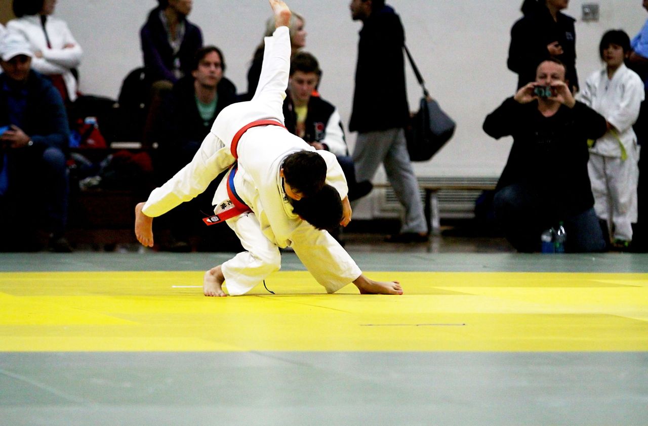 A junior judoka drives forward and down into a throw on the competition mat